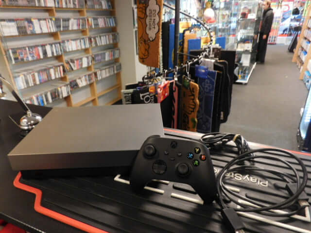 Xbox One X Console 1 TB with controller and cables on display in a game store.